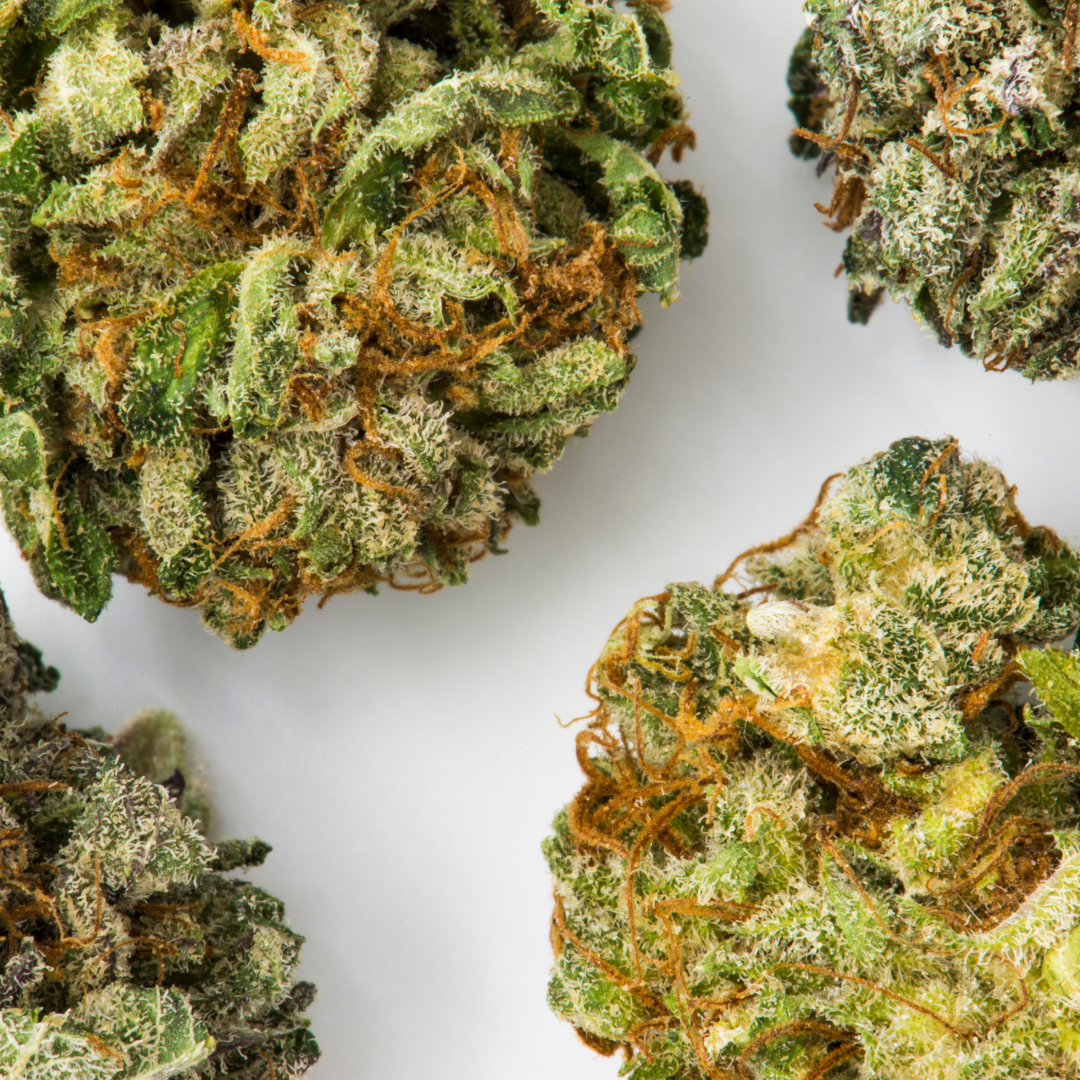 Close-up image of cannabis buds showcasing vibrant green leaves and orange pistils, highlighting the texture and density of the buds on a white background.