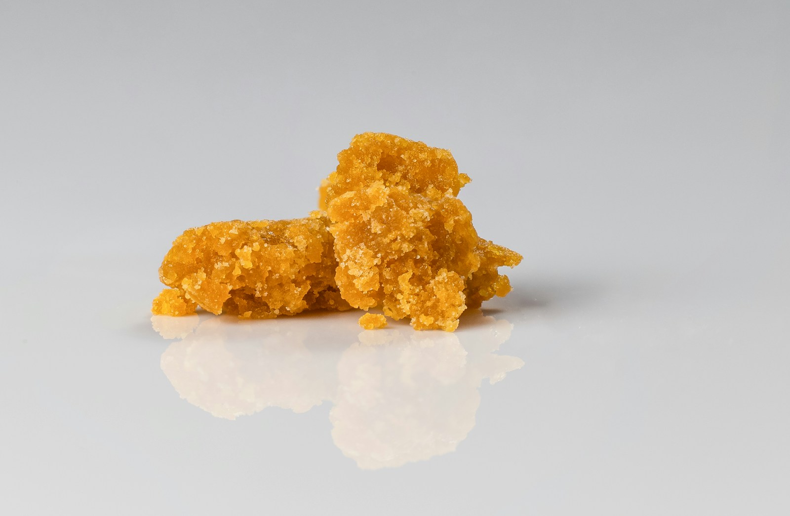 Close-up image of a clump of golden cannabis concentrate, showcasing its crystalline texture and reflective surface against a neutral background. Ideal for discussions on cannabis extraction methods and concentrate types.